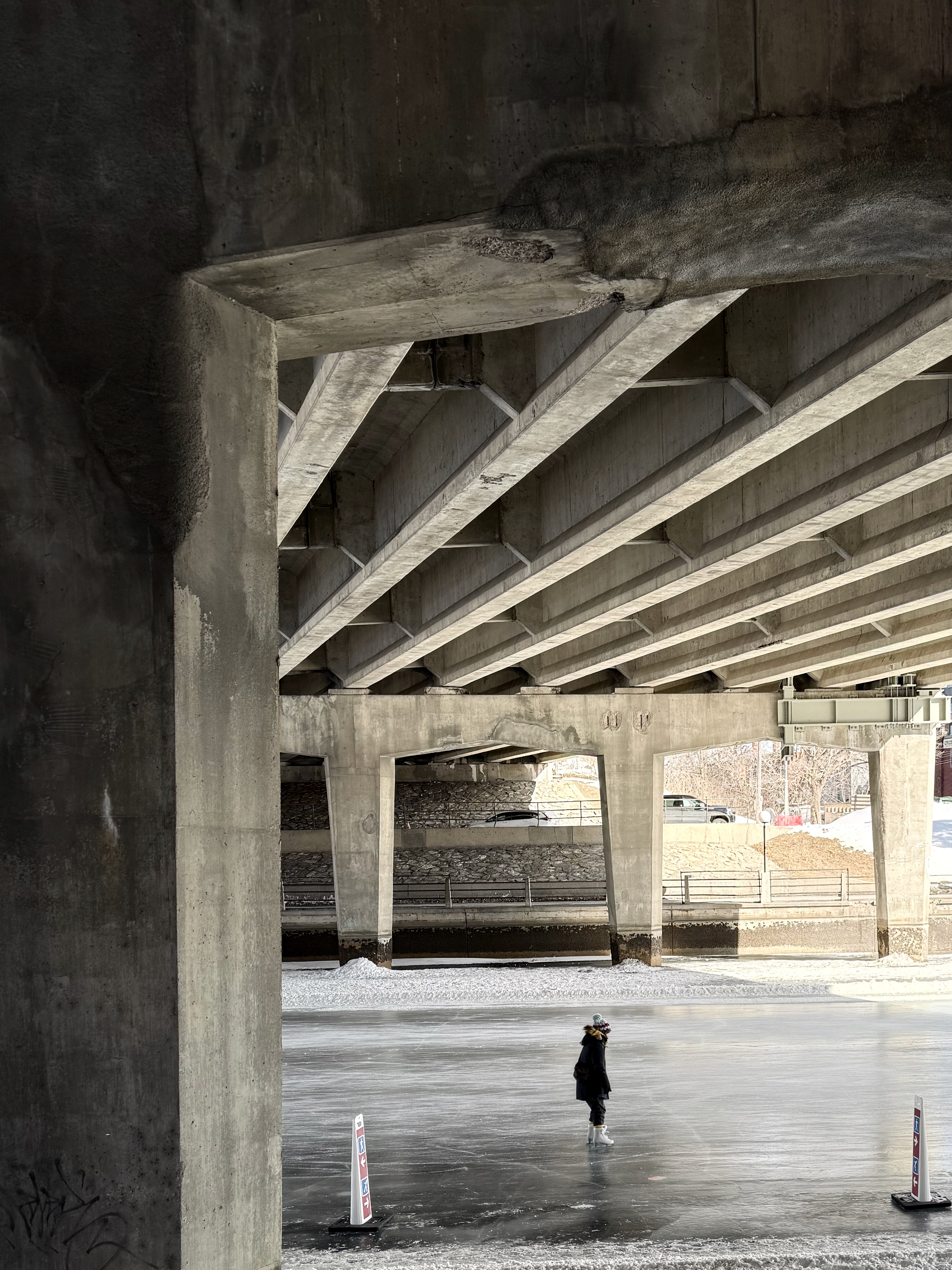 A person ice skating under a concrete bridge with graffiti and shadows.