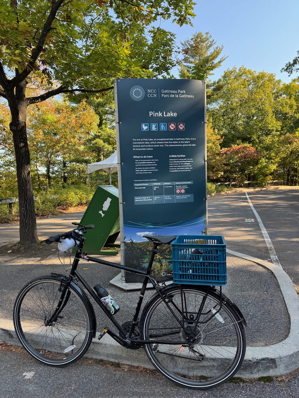 A bicycle in front of a sign. The sign reads Pink Lake, in Gatineau Park, QC