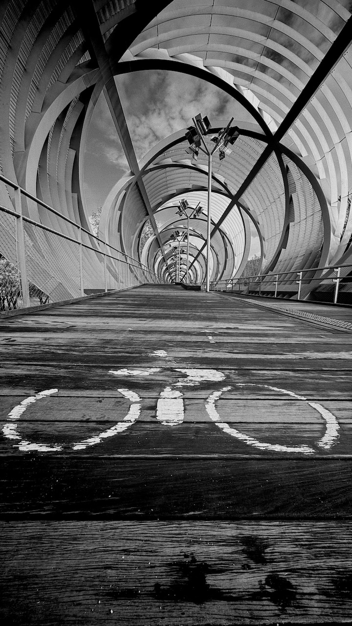 A cyclist in a tunnel with repeating arches and a bicycle lane marking.