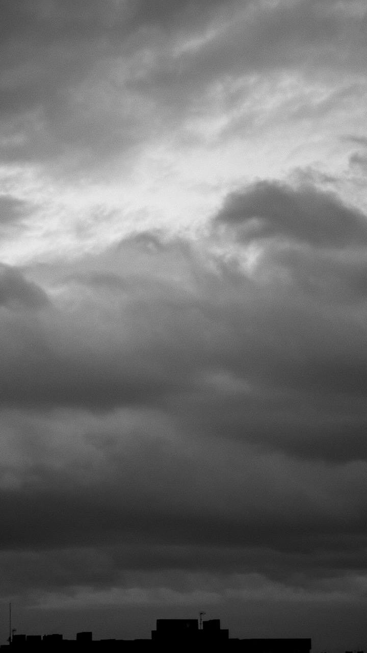 Silhouette of buildings under a dramatic, cloudy sky with light breaking through.