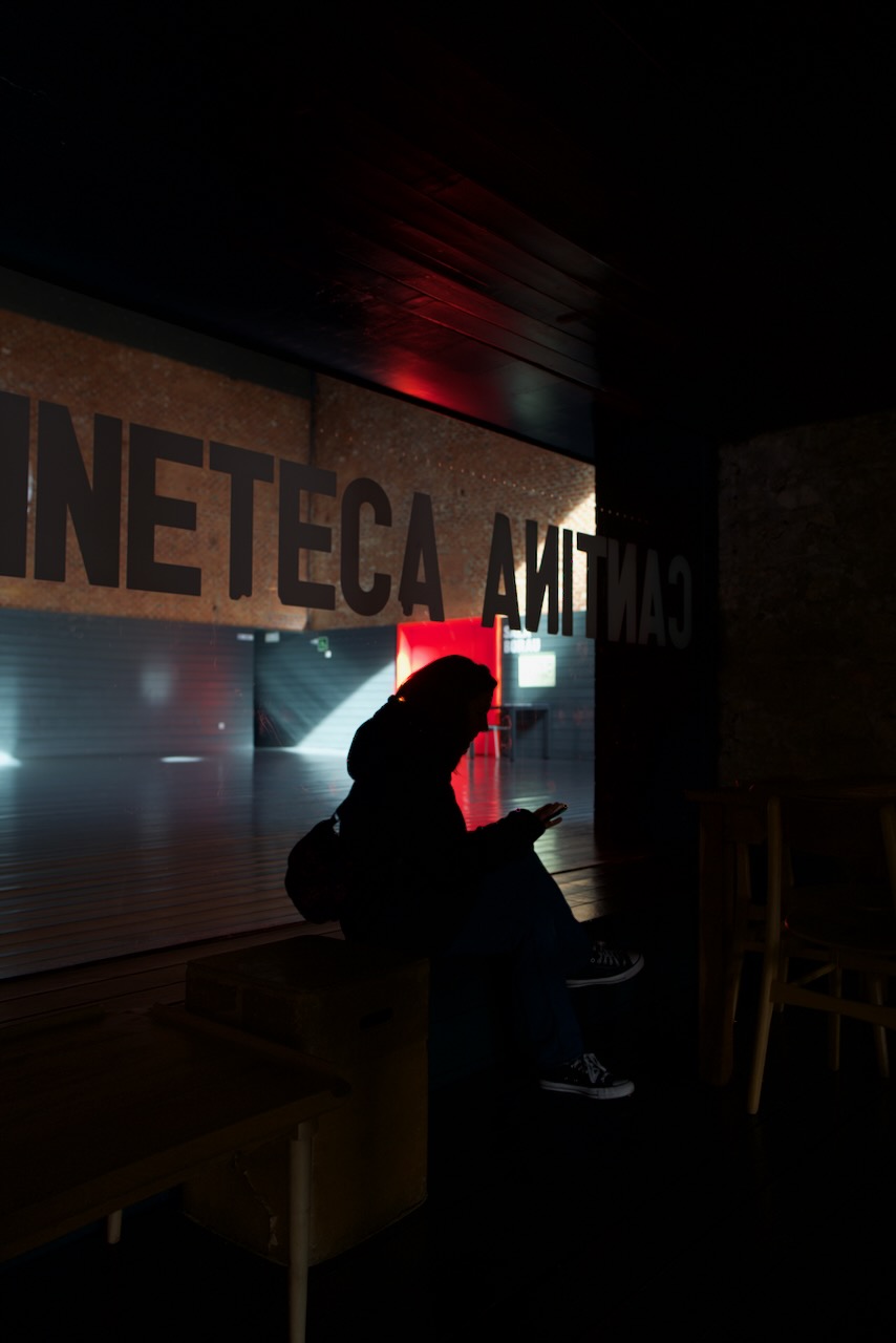 A person sitting in a dimly lit room, silhouetted against a window with illuminated text.